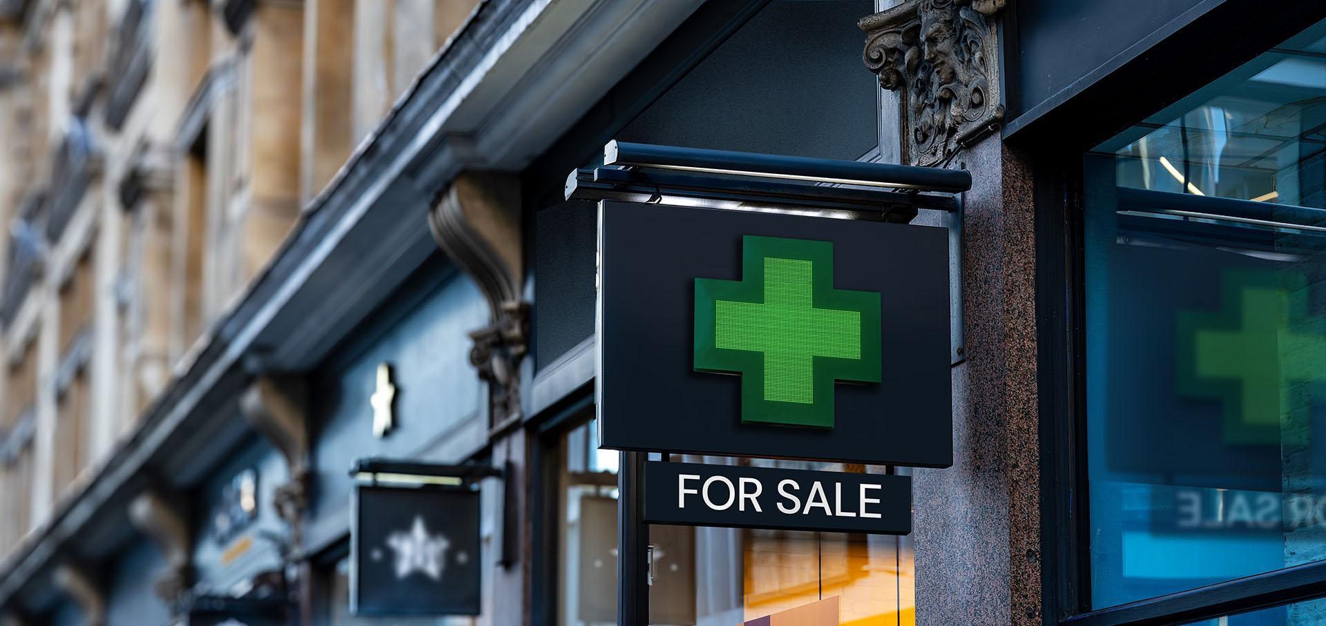 Outside green cross pharmacy sign with for sale sign